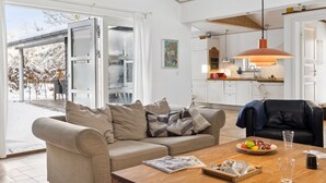 Una sala de estar moderna con un sofá color beige, una mesa de centro de madera y vistas a un área exterior nevada.