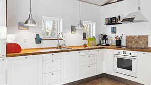 Una cocina moderna con armarios blancos, encimera de madera, horno empotrado y luces colgantes.