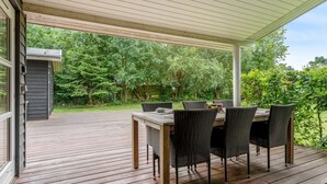 Un patio exterior cubierto con piso de madera, una mesa y sillas de mimbre.
