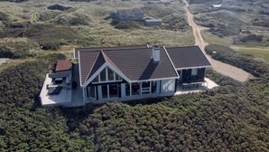 An aerial view of a modern house with a sloped roof, surrounded by dense vegetation and a dirt road. - "Rauli" - 50m from the sea by Interhome (Saltum)