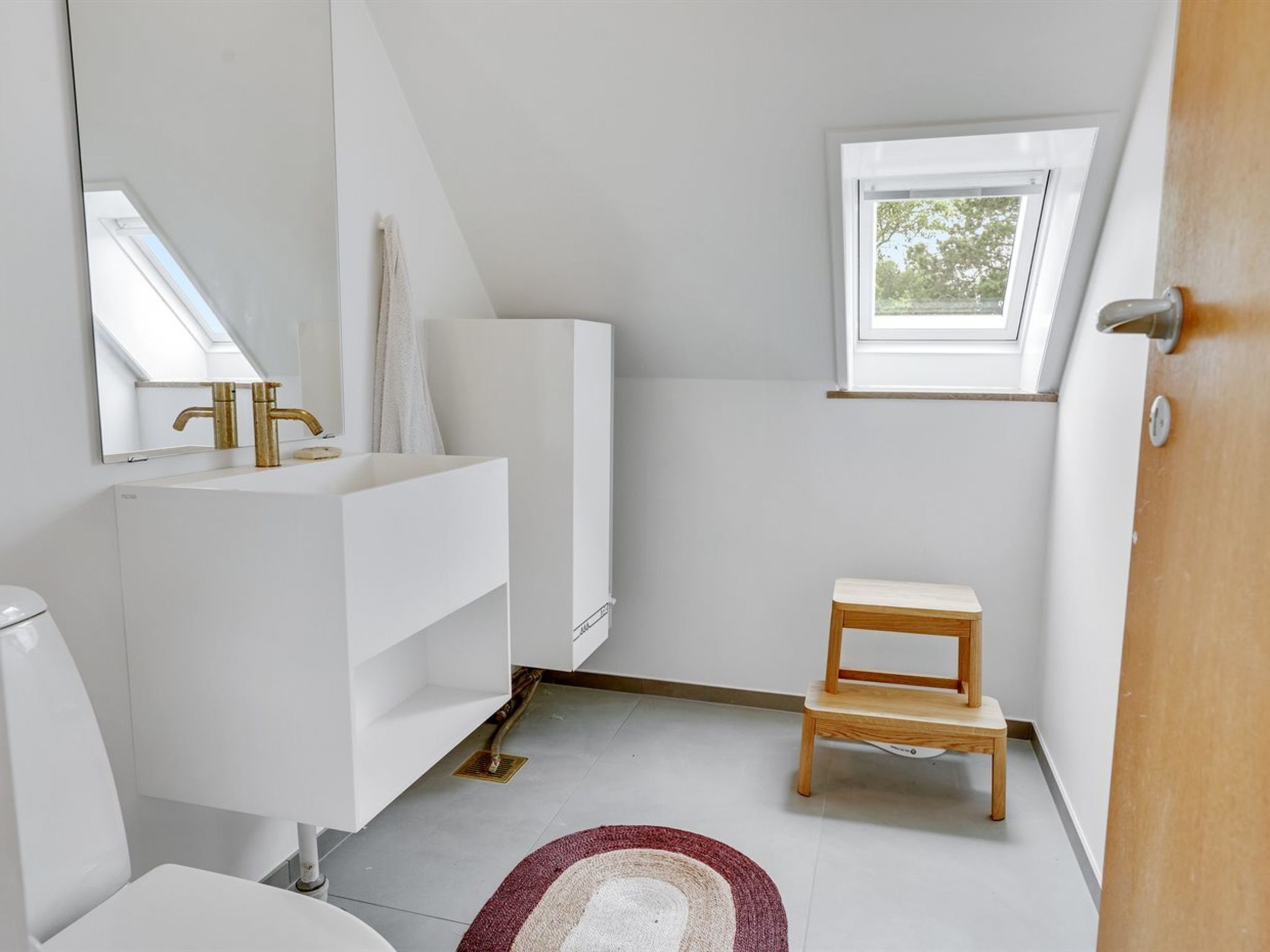 A modern bathroom with a white vanity, a wooden stool, a window, and a skylight.