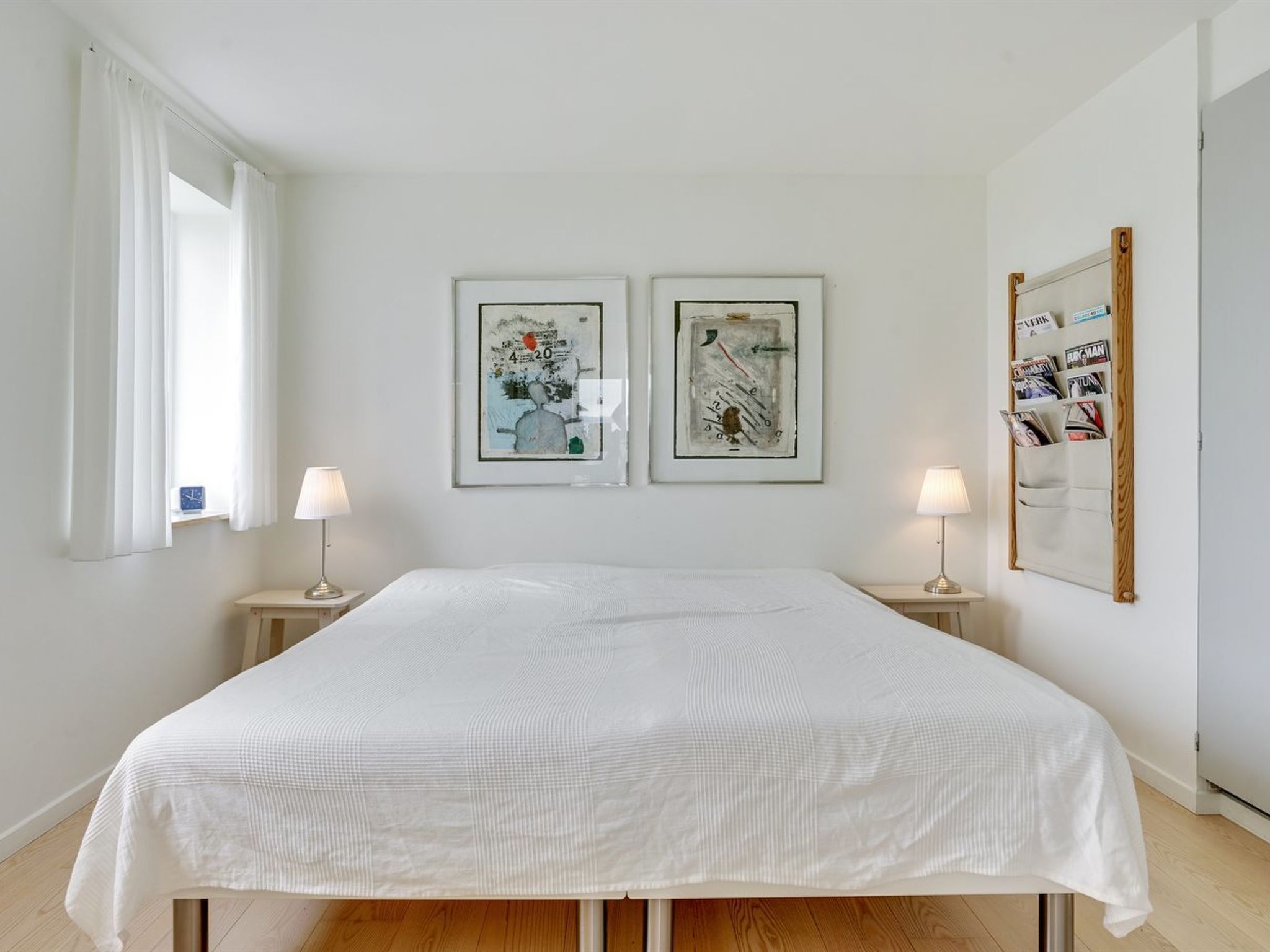 A bedroom with a large bed, two bedside tables with lamps, and two framed artworks on the wall.