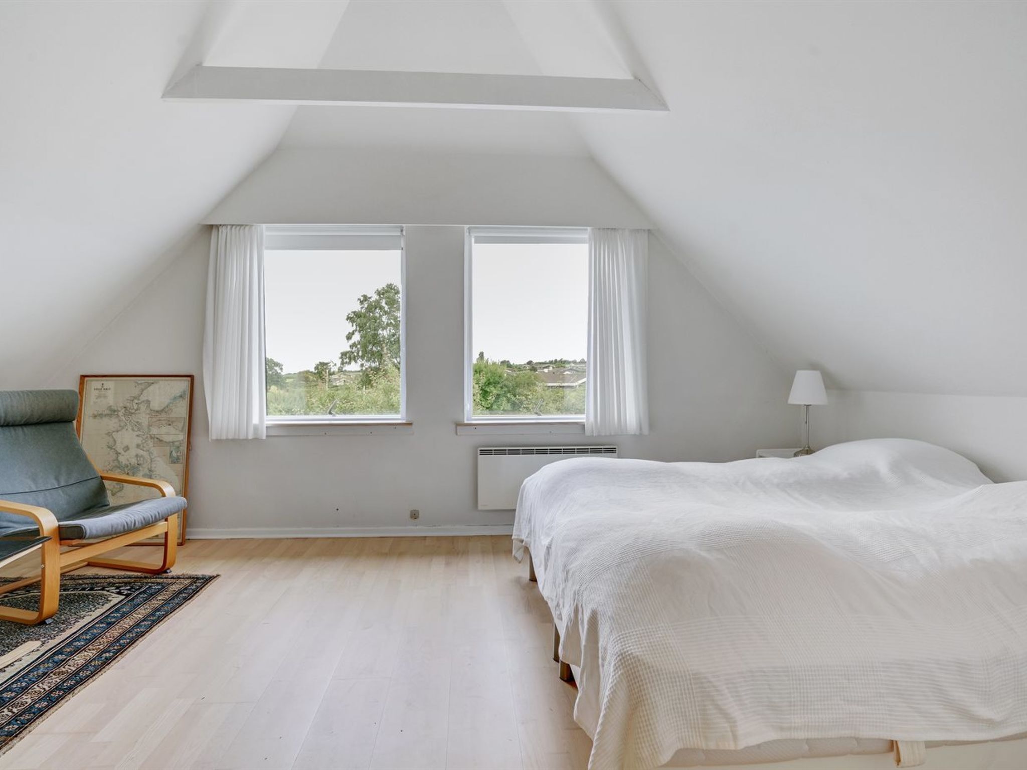 A bedroom with a bed, a chair, two windows, and a radiator.