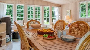 Un comedor de madera con una mesa grande, sillas de mimbre y una lámpara colgante.