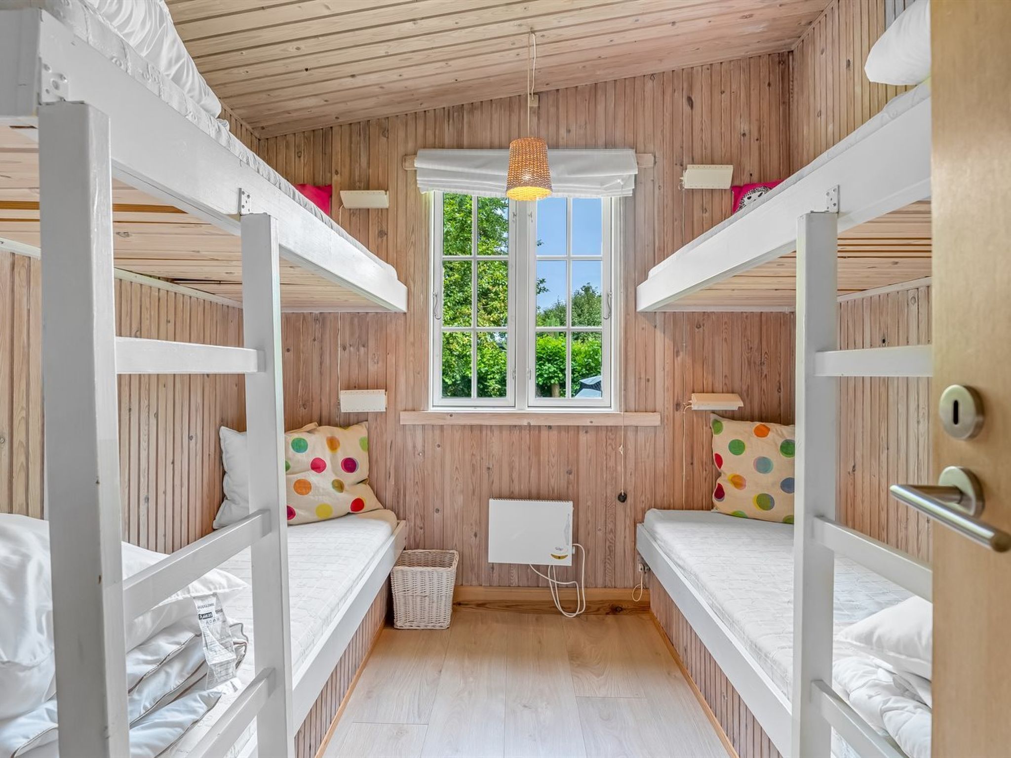 Une petite pièce avec des lits superposés, une fenêtre donnant sur un espace verdoyant et un petit radiateur blanc.