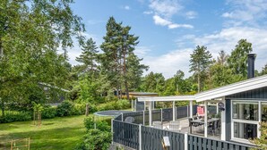 Eine moderne Außenterrasse mit überdachter Sitzgelegenheit, umgeben von einem gepflegten Garten und hohen Bäumen.