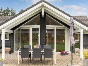 Ein überdachter Patio-Bereich mit Tisch und Stühlen, einer Glaseinfassung und einer Pergola mit Sonnenschirm.