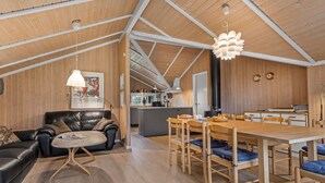 A modern interior with a wooden ceiling, a dining area with a wooden table and chairs, a black leather sofa, and a kitchen in the background.