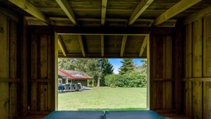 A room with a large bed, wooden beams, and a view of a house and lawn outside.