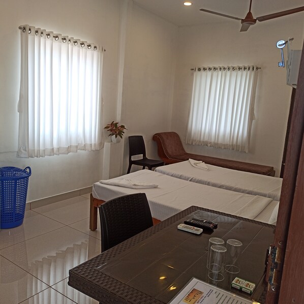 A hotel room with a bed, a desk with a chair, a blue basket, and a ceiling fan.