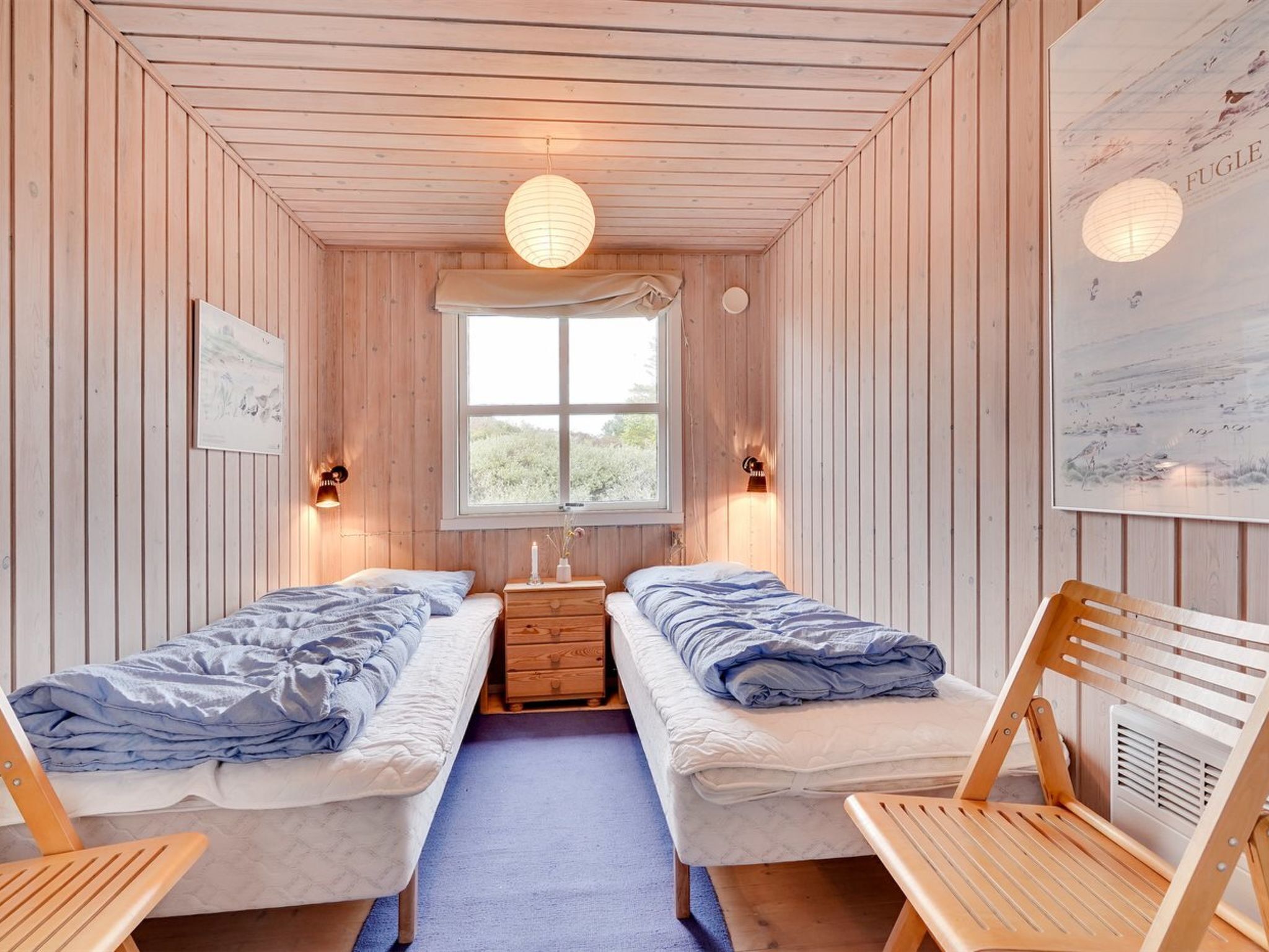 A cozy room with two beds, a window, and wooden walls.