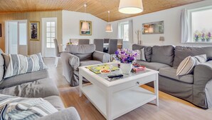 Een moderne woonkamer met een houten plafond, grijze banken, een witte salontafel en een groot raam met gordijnen.