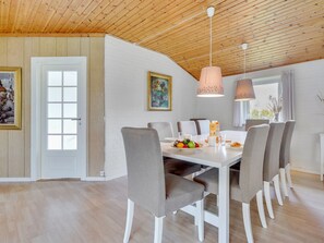 Un espace repas avec une table blanche, des chaises grises à revêtement en tissu et un plafond en bois.