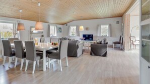 Een ruime woonkamer met een houten plafond, een eettafel met stoelen, een bank en een televisie.