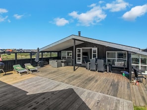 Una casa moderna con terraza de madera, mobiliario exterior y un amplio ventanal.