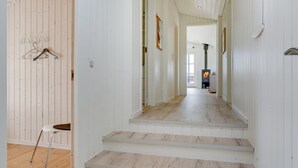 A hallway with wooden floors and white walls, leading to a room with a fireplace.