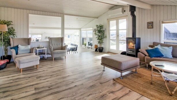 A spacious living room with a high ceiling, wooden flooring, a fireplace, and large windows allowing natural light.