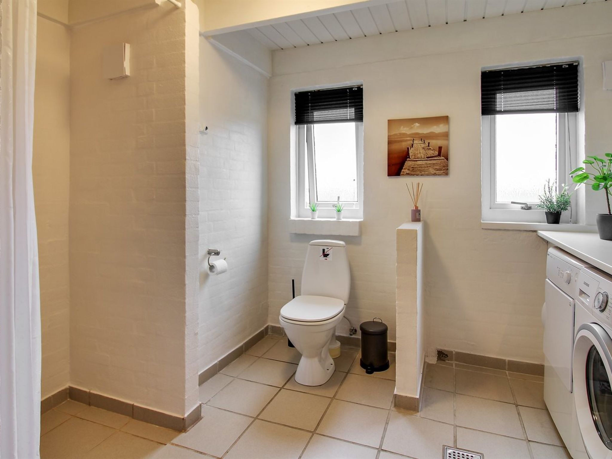 Une petite salle de bain comprenant des toilettes, un lave-linge et une fenêtre agrémentée d’une plante.