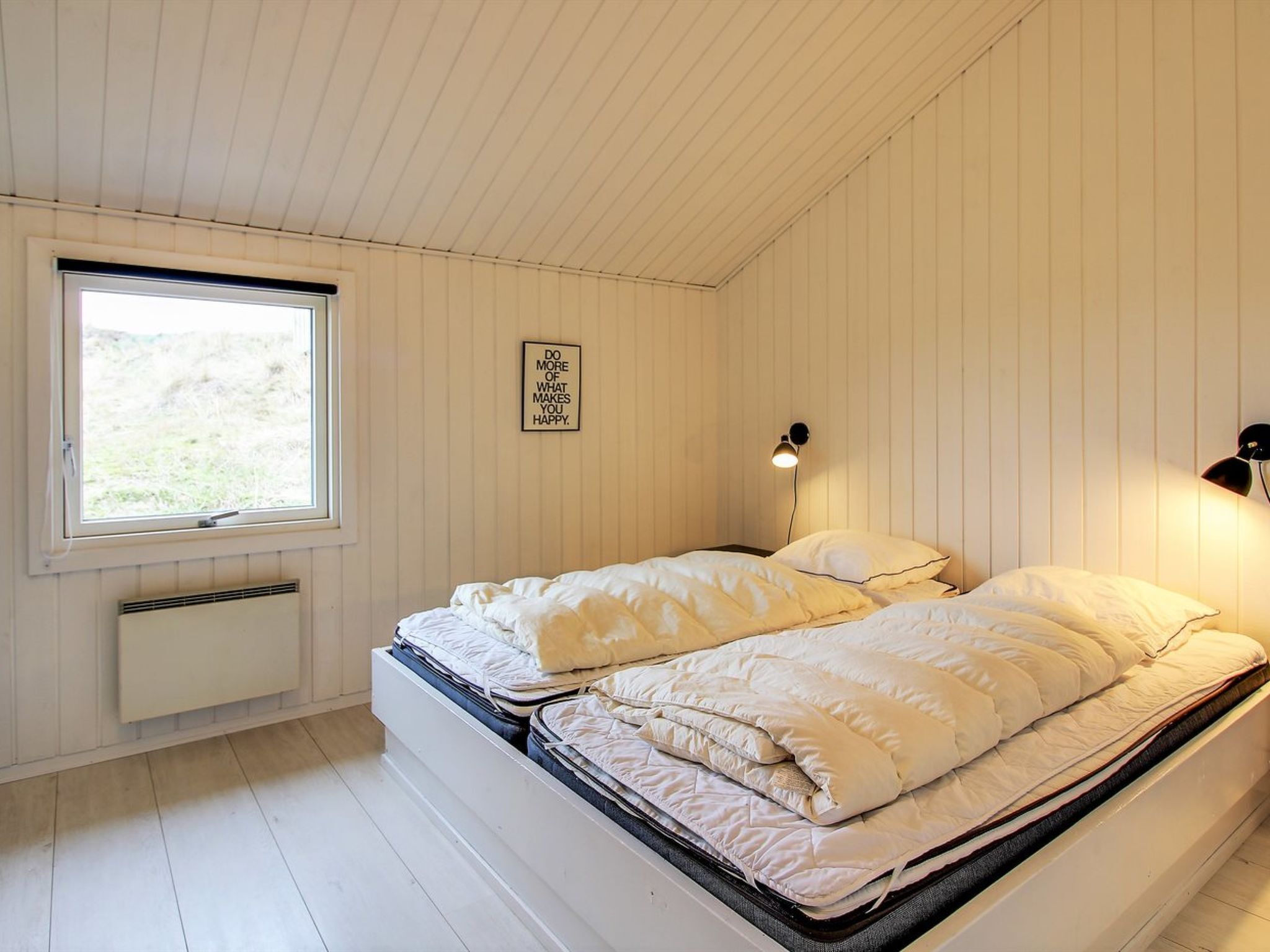 Une chambre avec un lit simple, une fenêtre, une lampe fixée au mur et une citation inspirante sur le mur.