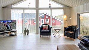A spacious living room with a large window, a television, and two leather sofas.