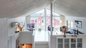 A spacious living area with a large TV, seating, and a view of a red building outside.