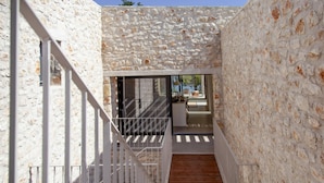 A narrow wooden staircase leading to a modern interior space with a stone wall and a glass door. - Theros Estate - Villa Aloe 1- 3 BED (Amfilochia)