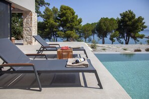 A poolside area with lounge chairs, a wooden table, and a bottle of wine. - Theros Estate - Villa Aloe 1- 3 BED (Amfilochia)