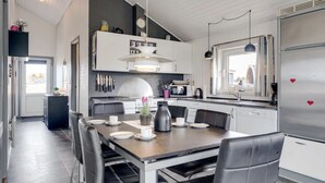 Una cocina moderna con armarios blancos, un refrigerador de acero inoxidable y un comedor con sillas negras y una mesa de madera.