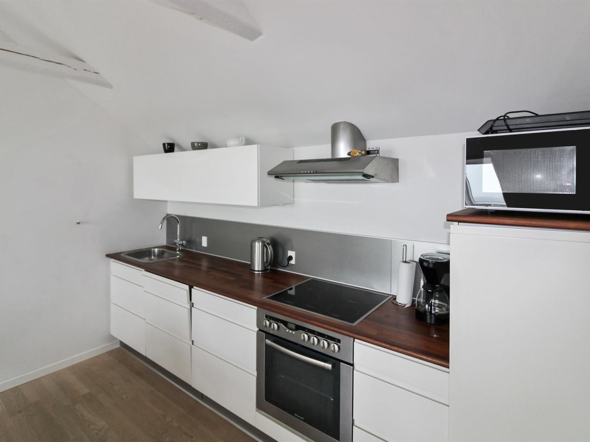 Eine moderne Küche mit weißen Schränken, einem Edelstahlbackofen, einer Mikrowelle und einem eingebauten Kochfeld.