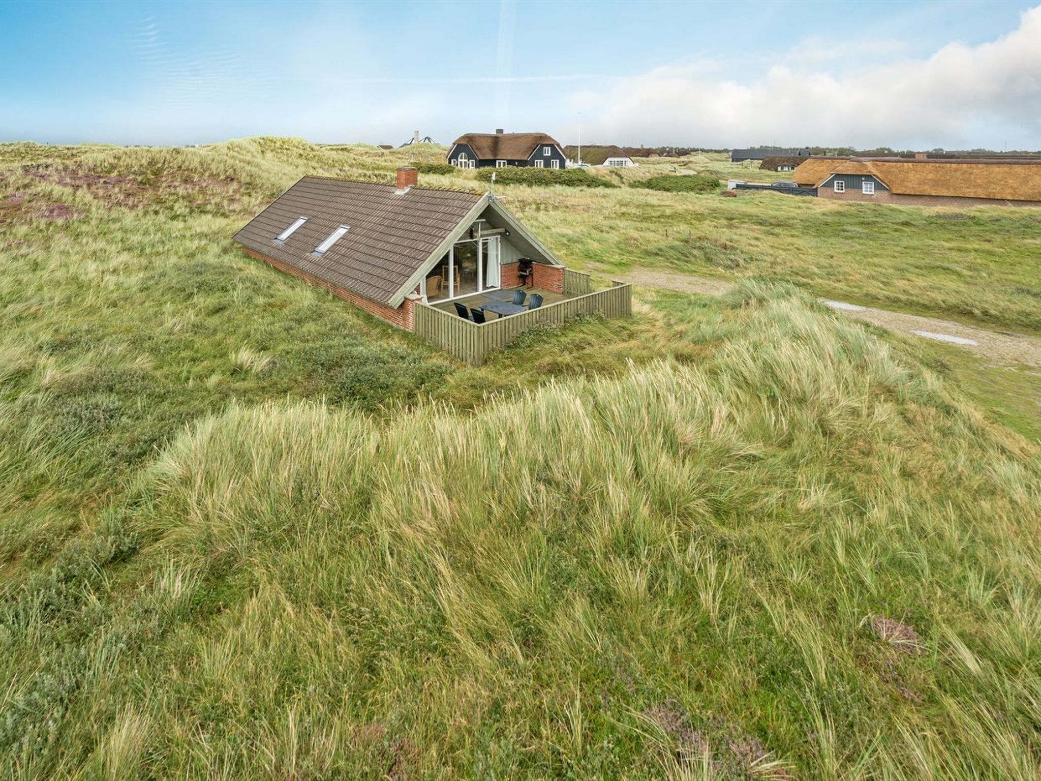 Une maison avec un toit en pente, une terrasse en bois et un champ verdoyant qui l’entoure.