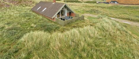 Une maison avec un toit en pente, une terrasse en bois et un champ verdoyant qui l’entoure.