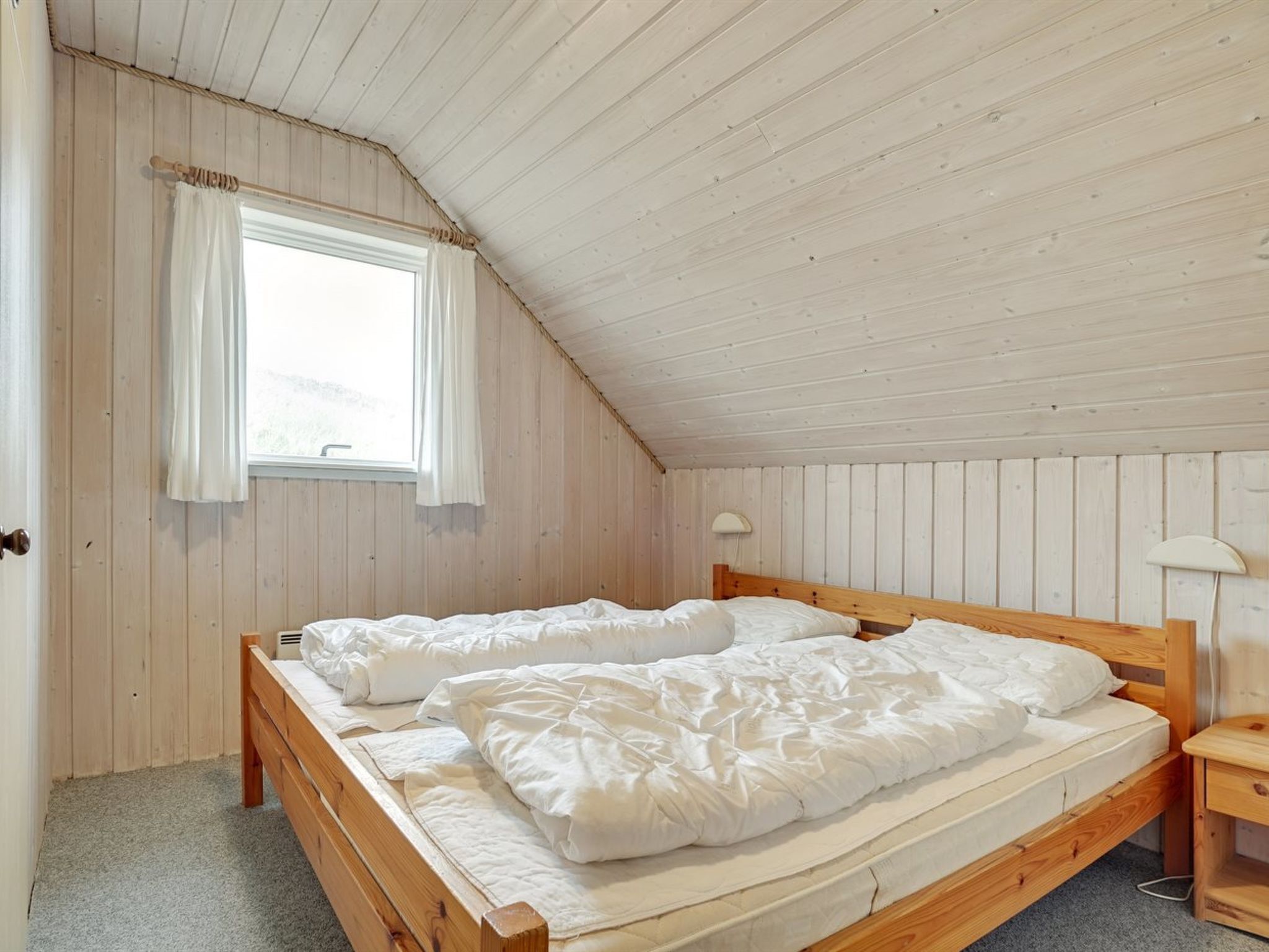 Een slaapkamer met twee houten bedden, een raam met gordijnen en een schuine kap.
