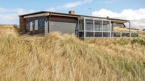 Une maison moderne avec une extension en verre, entourée d’herbes hautes.