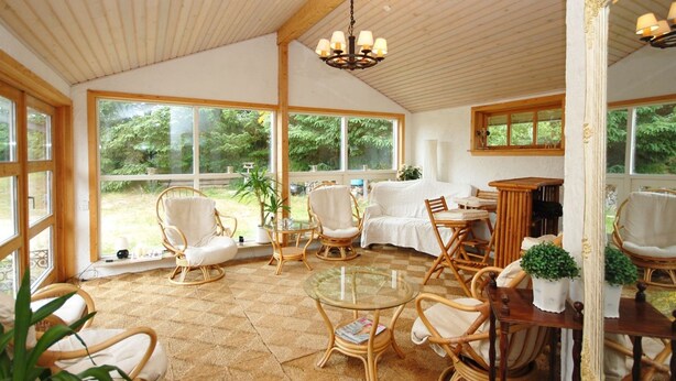 Une pièce lumineuse, baignée de soleil, avec de grandes fenêtres, des meubles en osier et une table en verre.
