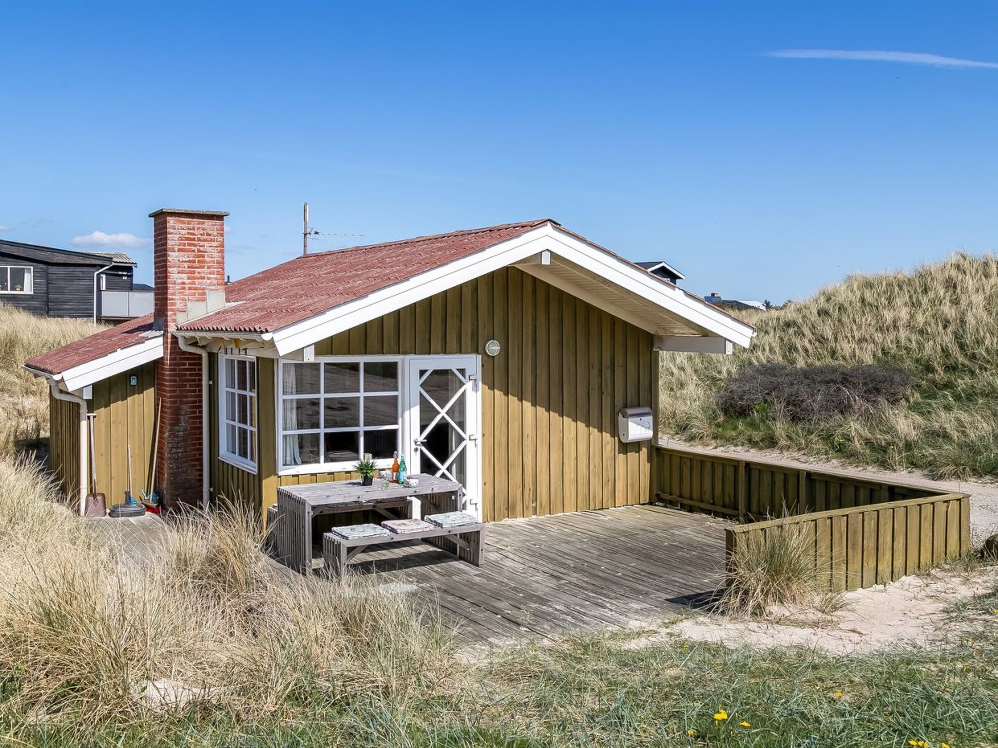 Une maison de plage en bois, avec un toit rouge, une terrasse en bois et une grande fenêtre.
