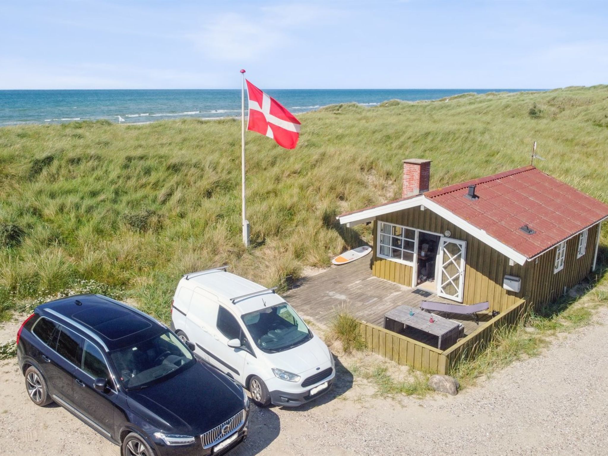 A small wooden building with a red roof, a flag, and a van parked in front.