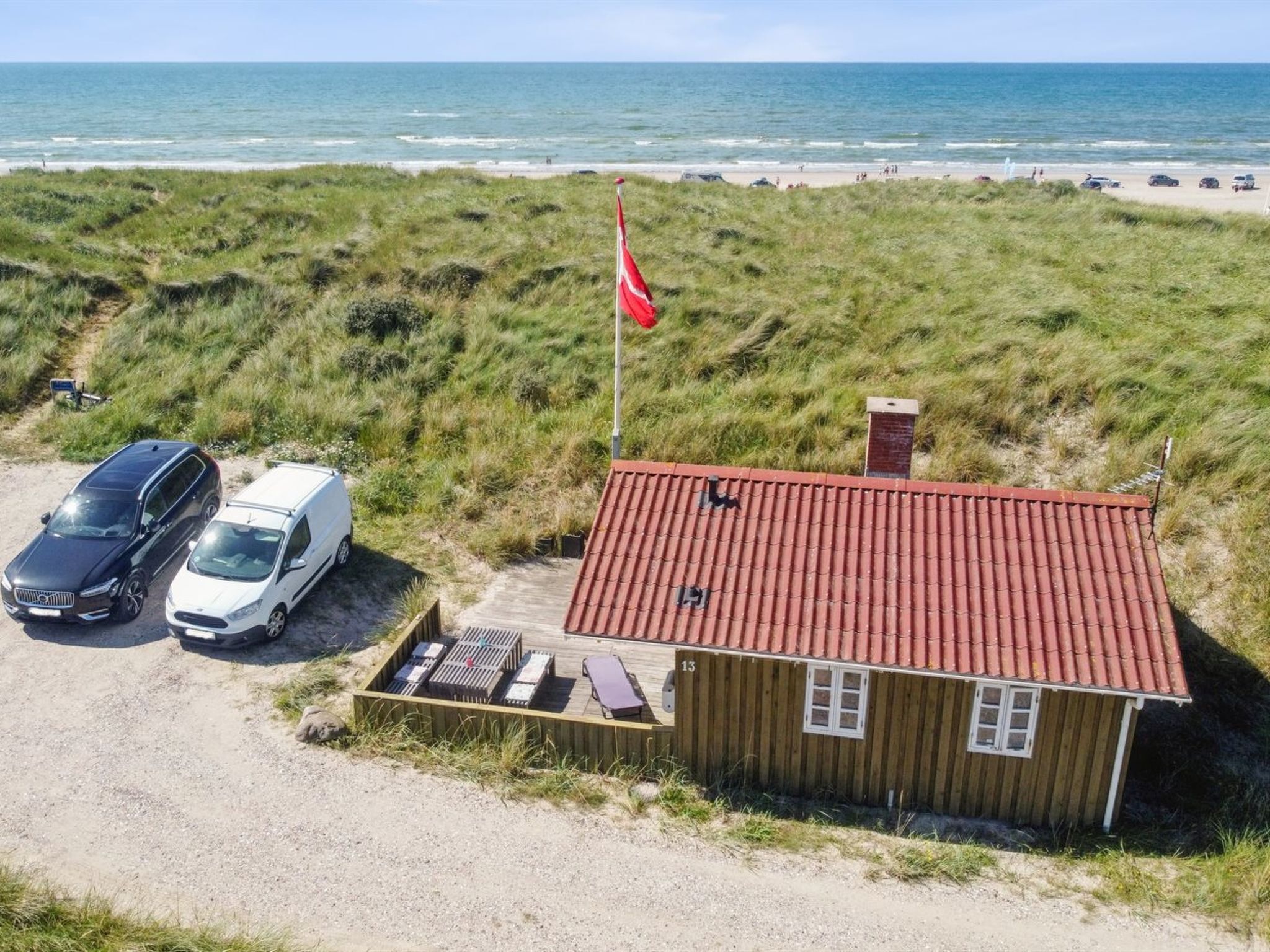 A coastal property with a red-roofed cabin, two parked cars, and a flagpole.