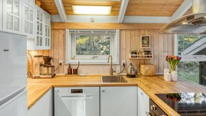 A modern kitchen with wooden cabinetry, a built-in dishwasher, a stove, and a window overlooking a garden. - "Berenice" - 250m from the sea by Interhome (Hals)