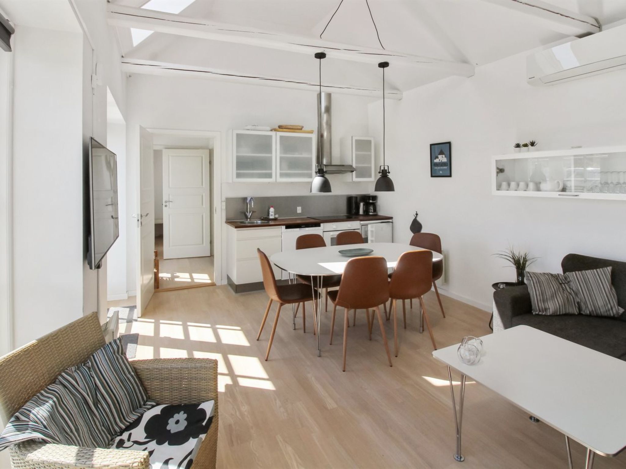 A spacious living area with a dining table, chairs, a sofa, and a kitchen with cabinets and a sink.