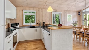 Une cuisine moderne avec un lambris en bois, un îlot central et de grandes fenêtres offrant une vue sur la verdure.