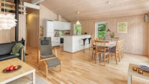 Un vaste espace de vie doté d’un plancher en bois, d’une table à manger avec des chaises, d’un canapé et d’un coin cuisine avec des meubles blancs et une cuisinière.