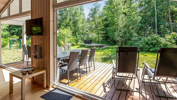 Un intérieur moderne avec une terrasse en bois, un coin repas comprenant des chaises et une table, et un téléviseur fixé au mur.