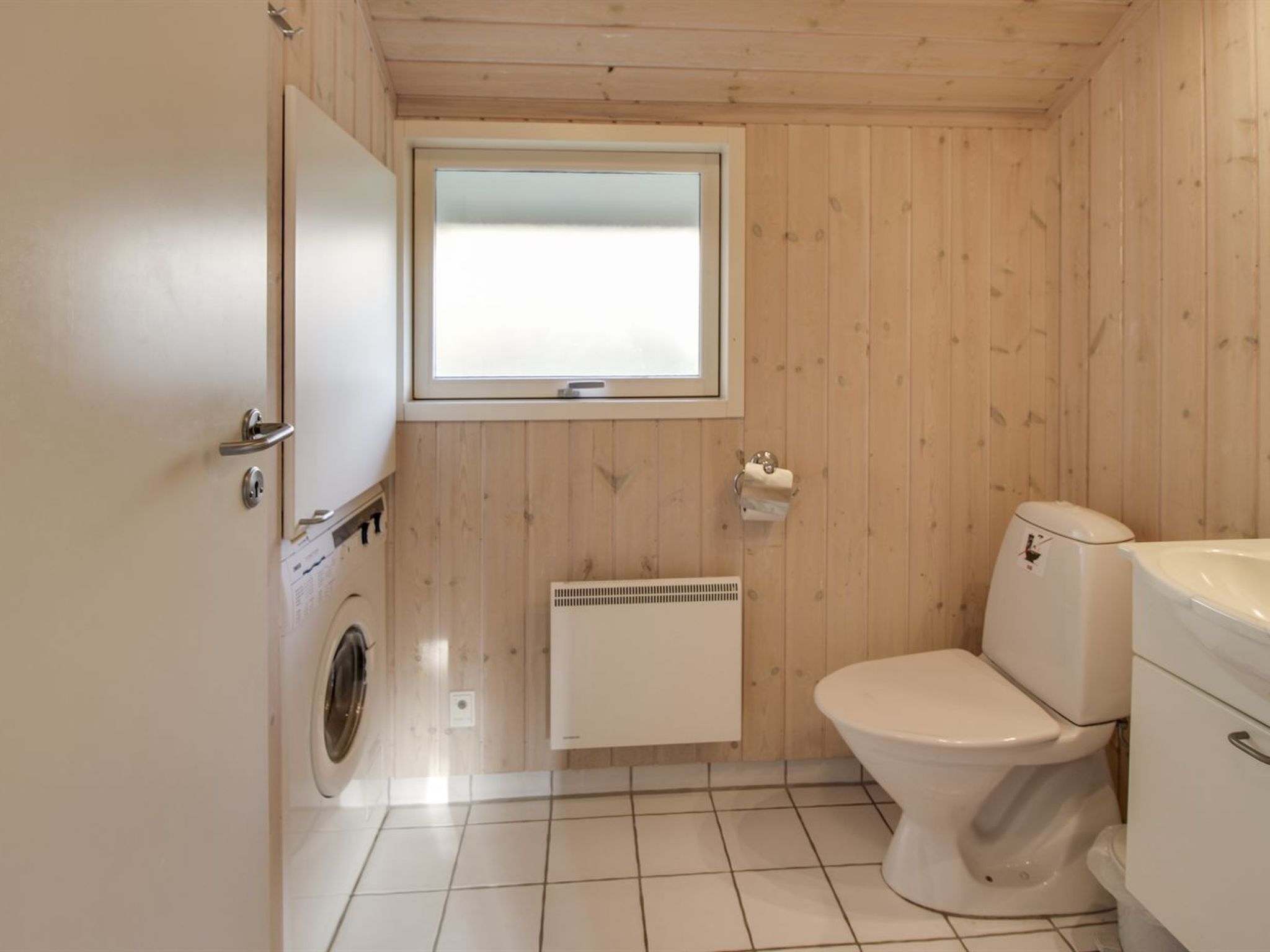 A compact bathroom with a toilet, a washing machine, and a window.