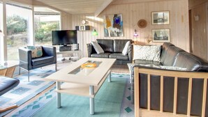 A spacious living room with a wooden ceiling, a television, a sofa, a coffee table, and a view of the outdoors.