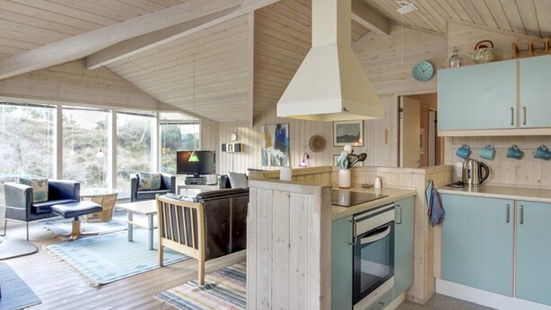 A modern kitchen with wooden cabinets, a built-in oven, and a dining area with a sofa and table.