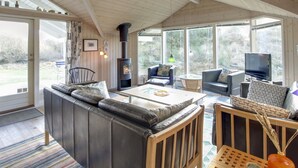 A cozy living room with a fireplace, comfortable seating, and large windows offering a view of the outdoors.