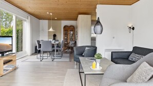 A modern living room with a wooden ceiling, a dining area with a glass cabinet, and a large window providing a view of greenery. - "Onni" - 1km from the sea by Interhome (Væggerløse)