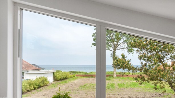 A room with a large window offering a view of a coastal landscape, including a tree and a grassy area. - "Biorn" - 70m from the sea by Interhome (Otterup)