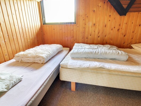 Two single beds with white bedding in a wooden cabin room with a sloped ceiling and a window.