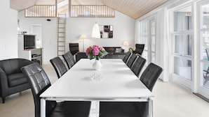 Un comedor moderno con una mesa blanca, sillas de cuero negro y un florero con flores.